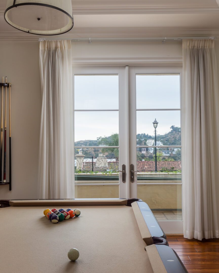 A pool table with white curtains and a view of the city.